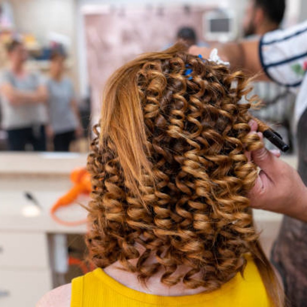 Close up hands of a hairdresser and treatment to a curly red hair woman. High quality photo